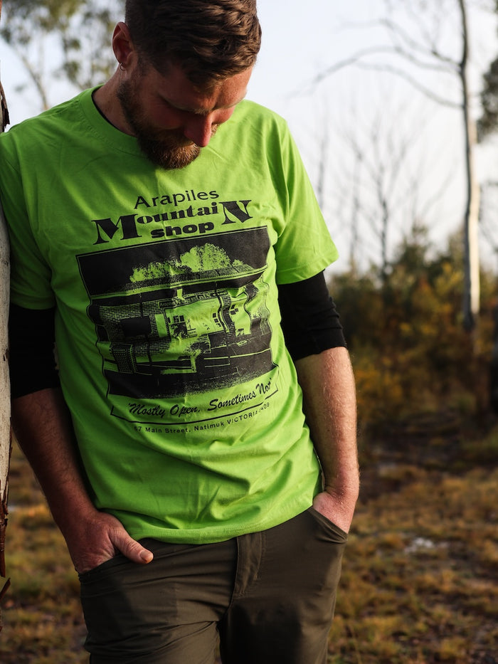 Person wearing a bright green t-shirt with 'Arapiles Mountain Shop' printed on it, standing outdoors.