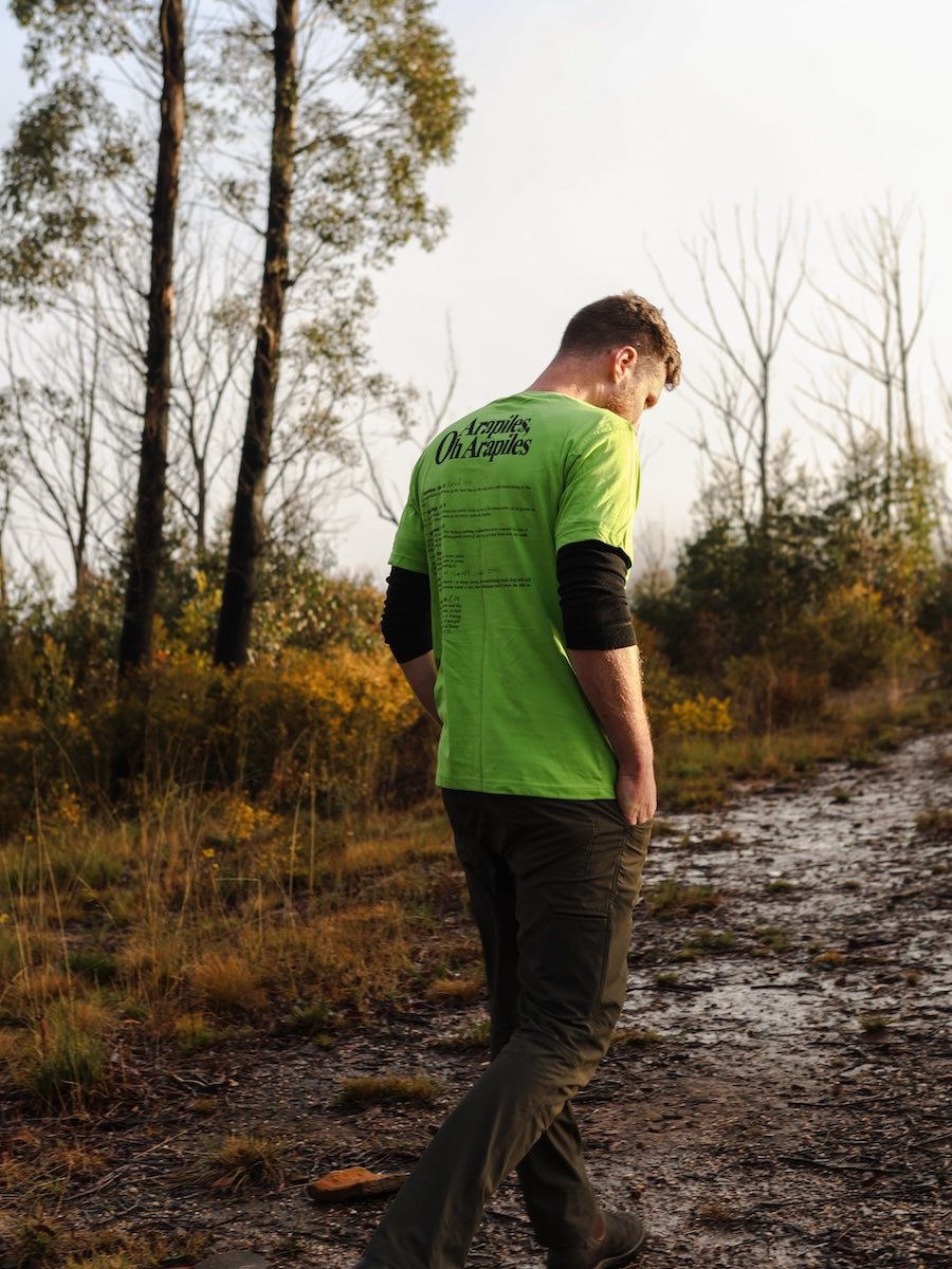 Person wearing a bright green shirt with text walking on a dirt path in a forest.