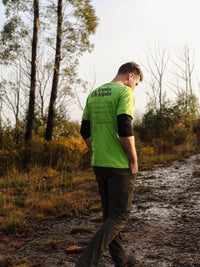 Person wearing a bright green shirt with text walking on a dirt path in a forest.