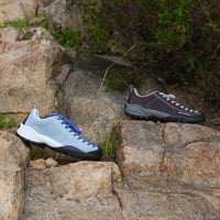 Two climbing shoes on a rocky surface with greenery.