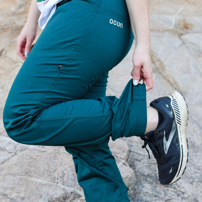 Person wearing teal pants with 'ocon' branding, standing on a stone surface.