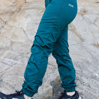 Teal pants with 'ocun' branding worn by a person on a stone surface